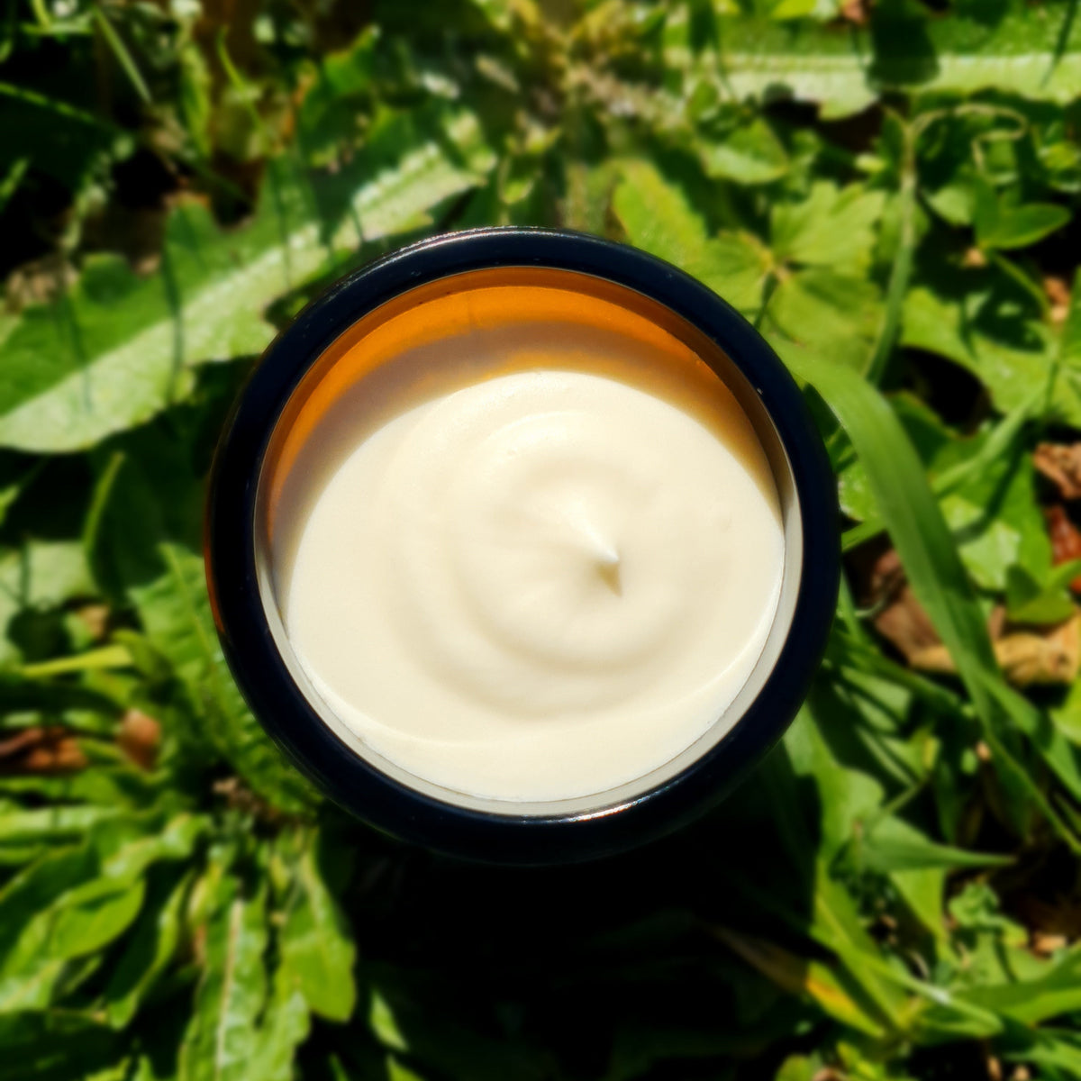 An open jar of tallow whip with a dark rim, placed on green grass outdoors.